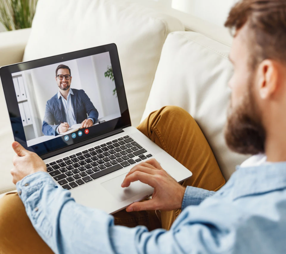Junger Mann in einer Online Videokonferenz mit Laptop im Schoß
